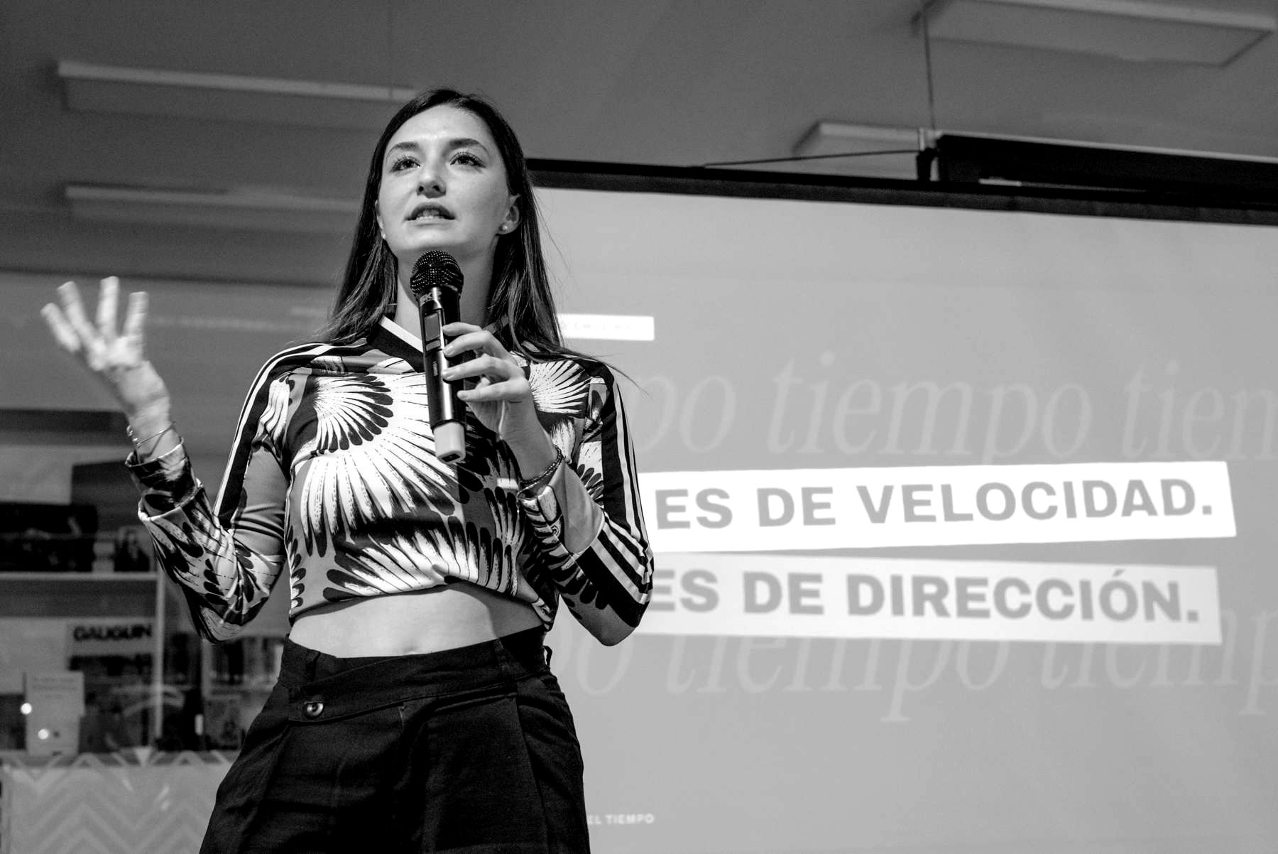 María Jesús Abril de pie dando una charla con micrófono, frente a una pantalla proyectada.