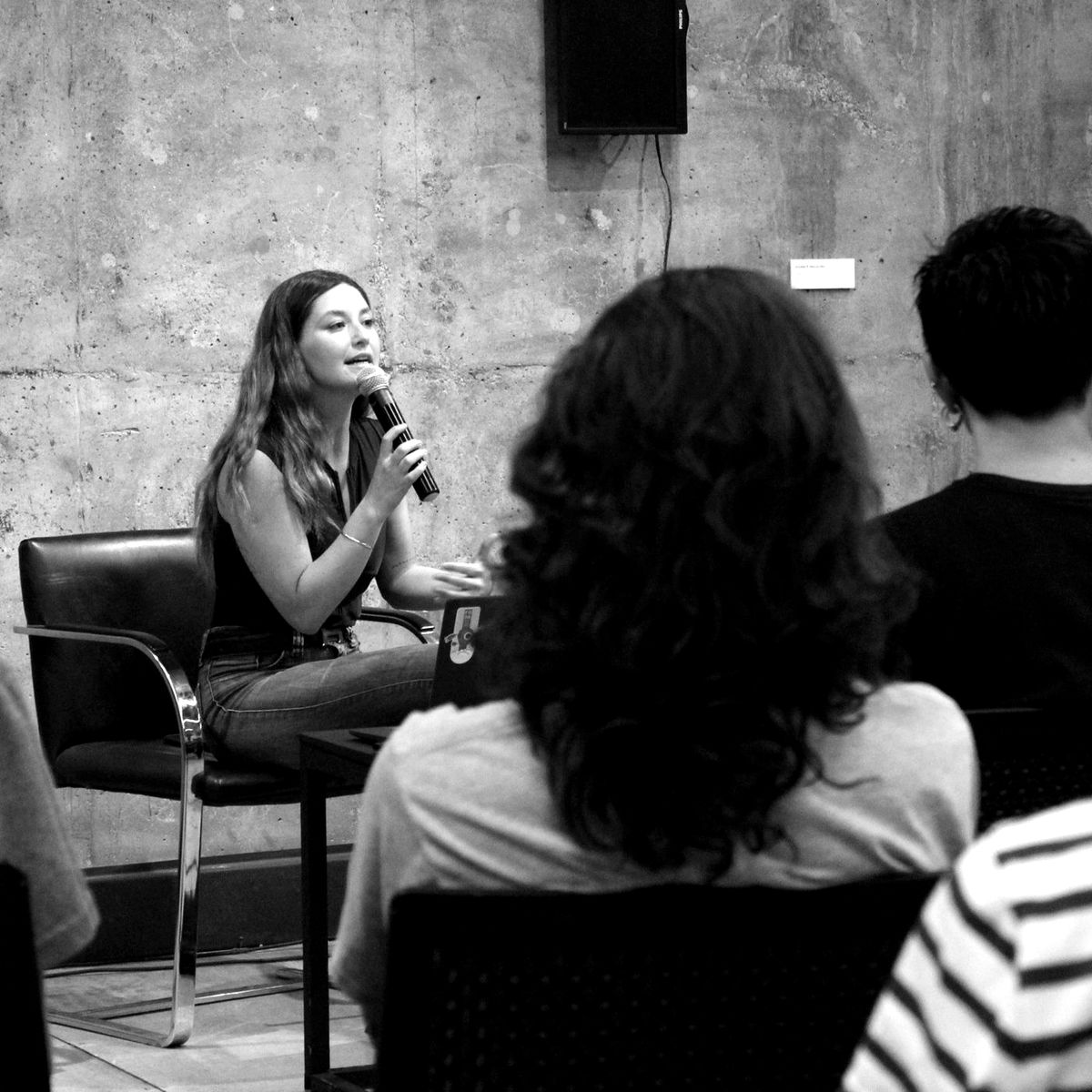 María Jesús Abril sentada, hablando con un micrófono frente al público.